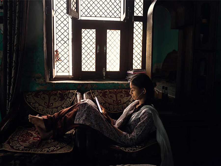 A young woman sits in front of a window, engrossed in a book.