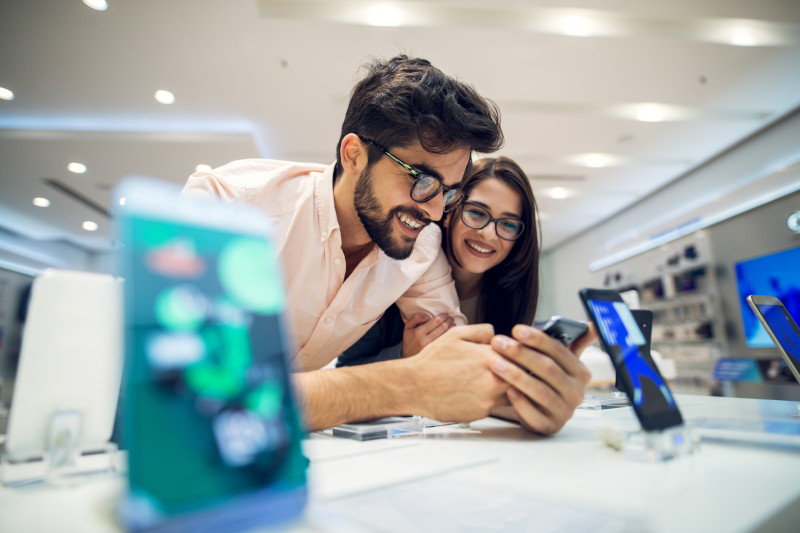 Homme et femme penchés sur un bureau, souriant en regardant quelque chose sur le téléphone