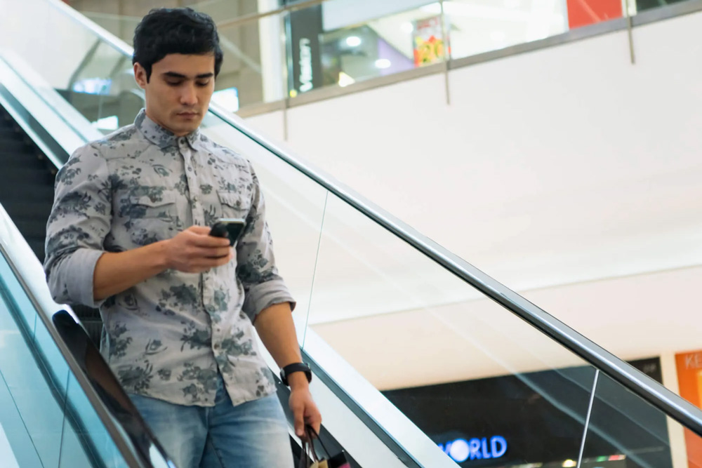 Un homme descend un escalier mécanique dans un centre commercial en regardant son téléphone