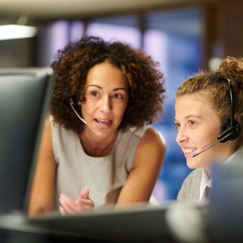 Two women with headsets observing the computer monitor in front of them