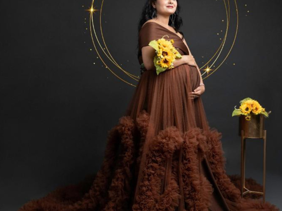 A pregnant woman holding sunflowers and standing in front of a dark background