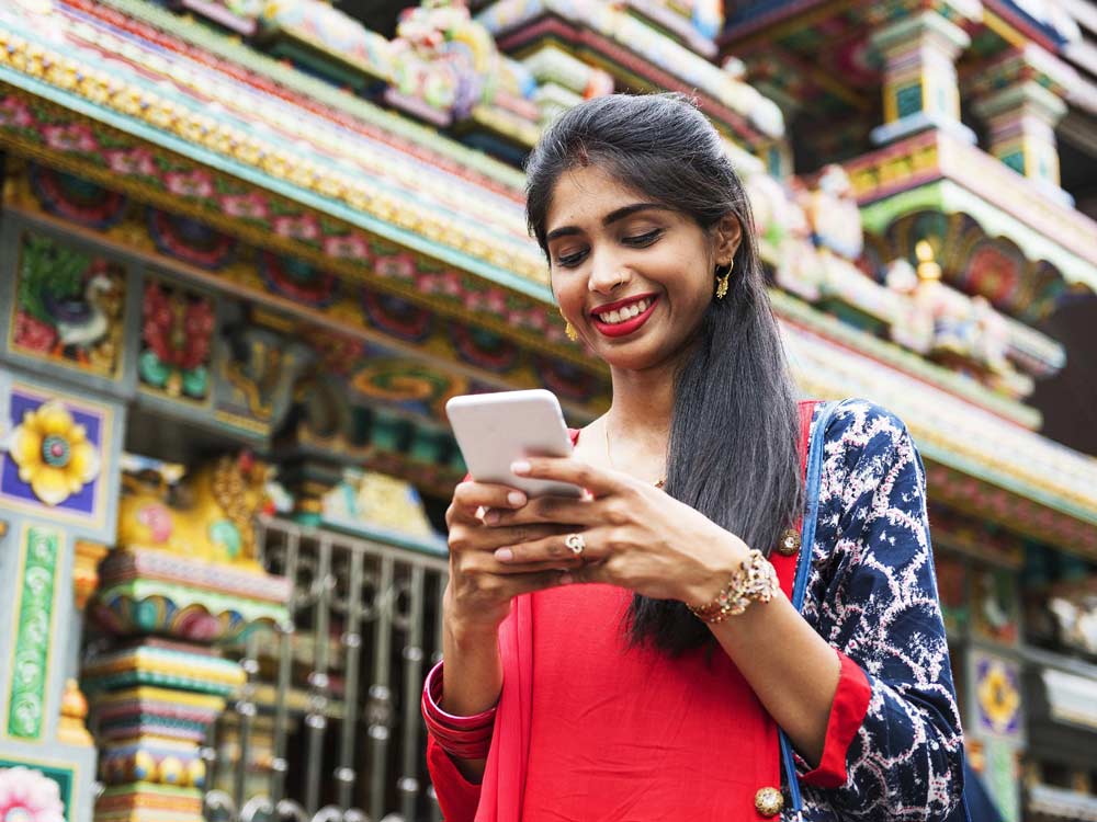A woman outside smiling while looking down at her cell phone