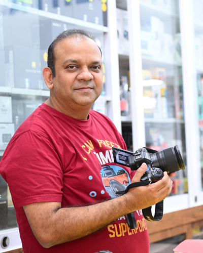 A man in his store holding his camera