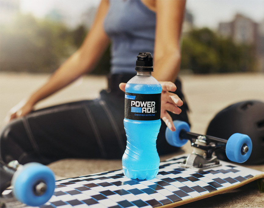 A woman grabbing her powerade drink that's sitting on top of a skateboard