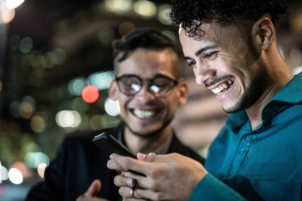 Deux hommes souriant et regardant l’un de leurs téléphones