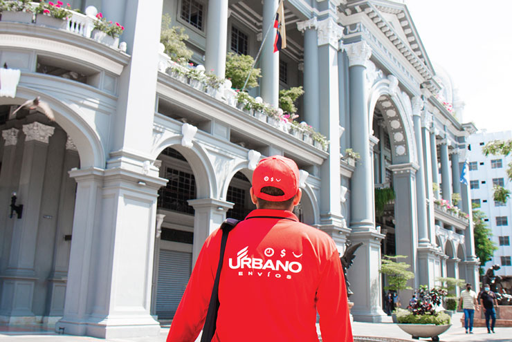 An Urbano Envios delivery man in front of an historical building