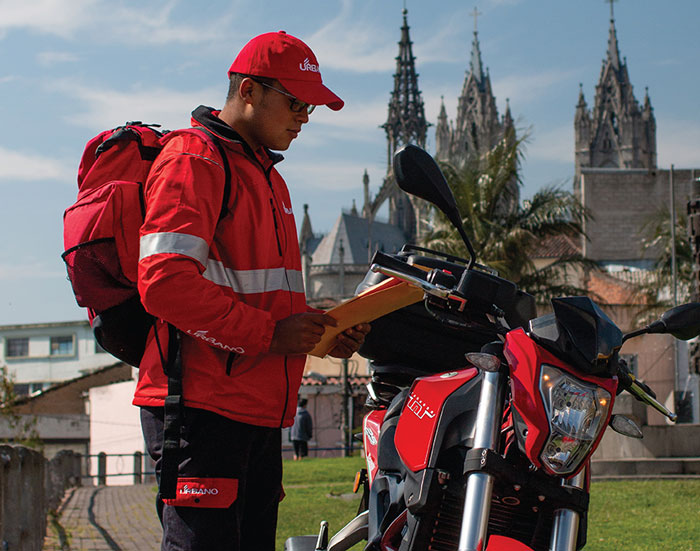 A Urbano Envios delivery man standing next to a motorcycle