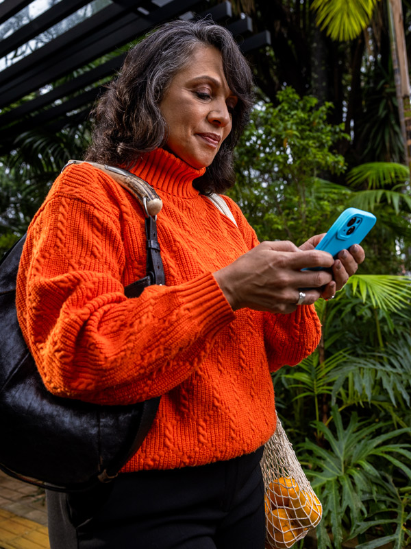 A woman holding a cellphone and bag, walking down the street
