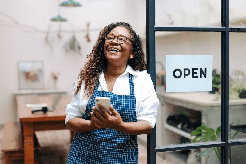 A woman working and smiling, next to an open sign