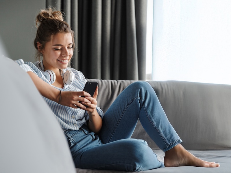Women with headphones on sitting on a couch looking at her phone