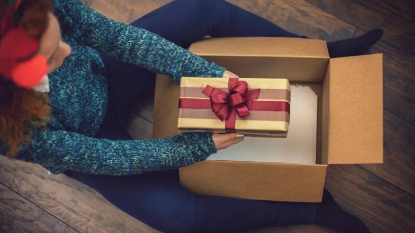 Personne assise par terre déballant un paquet cadeau
