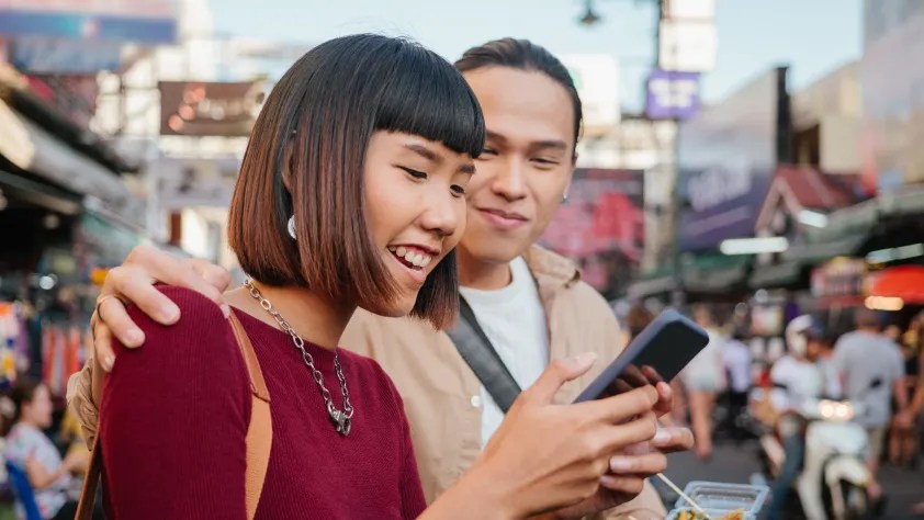 Dua orang di tengah pasar jalanan tersenyum melihat telepon