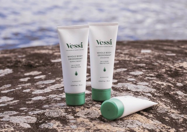 Three tubes of Vessi deodorant on a rocky surface near water