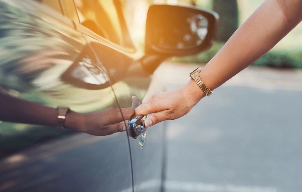 A persons hand reaching to open a car door handle