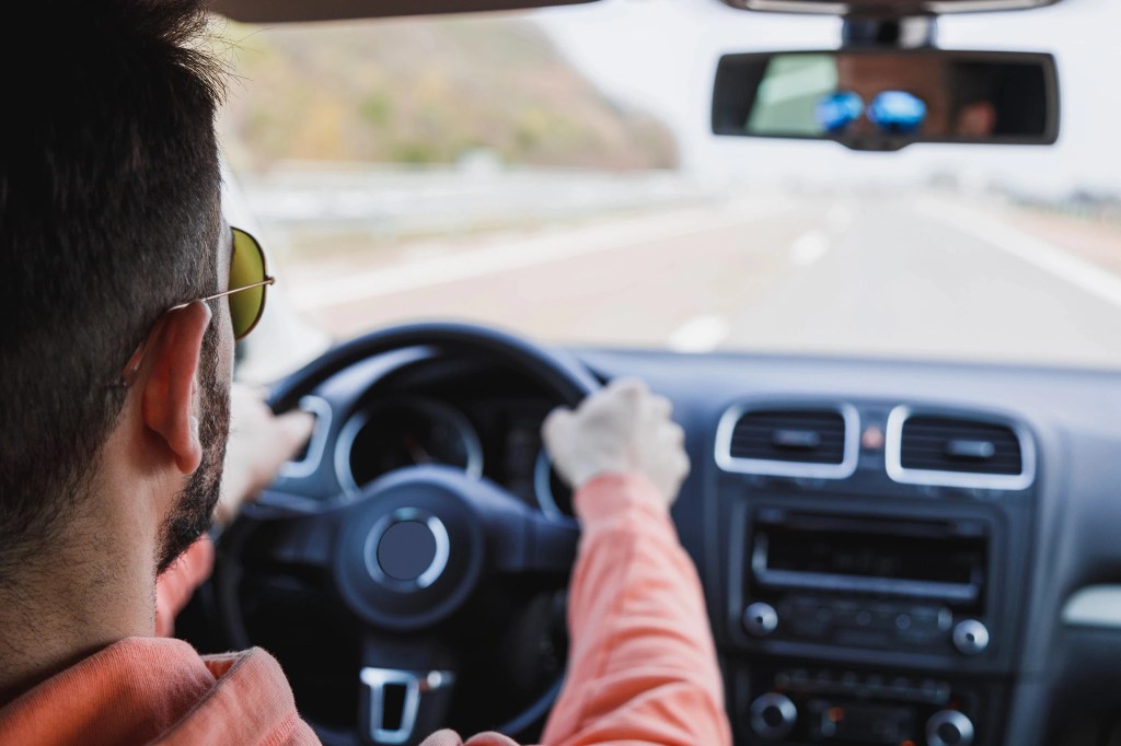 View of a man in the drivers seat of a car with both hands on the wheel