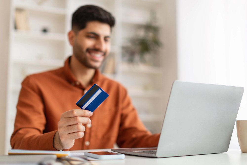 Homem segurando um cartão de crédito enquanto olha para o notebook