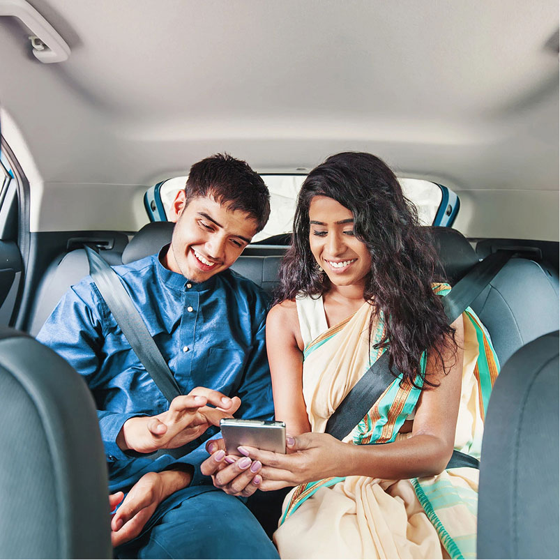 Two uber passengers sitting in the back seats looking at their phone.
