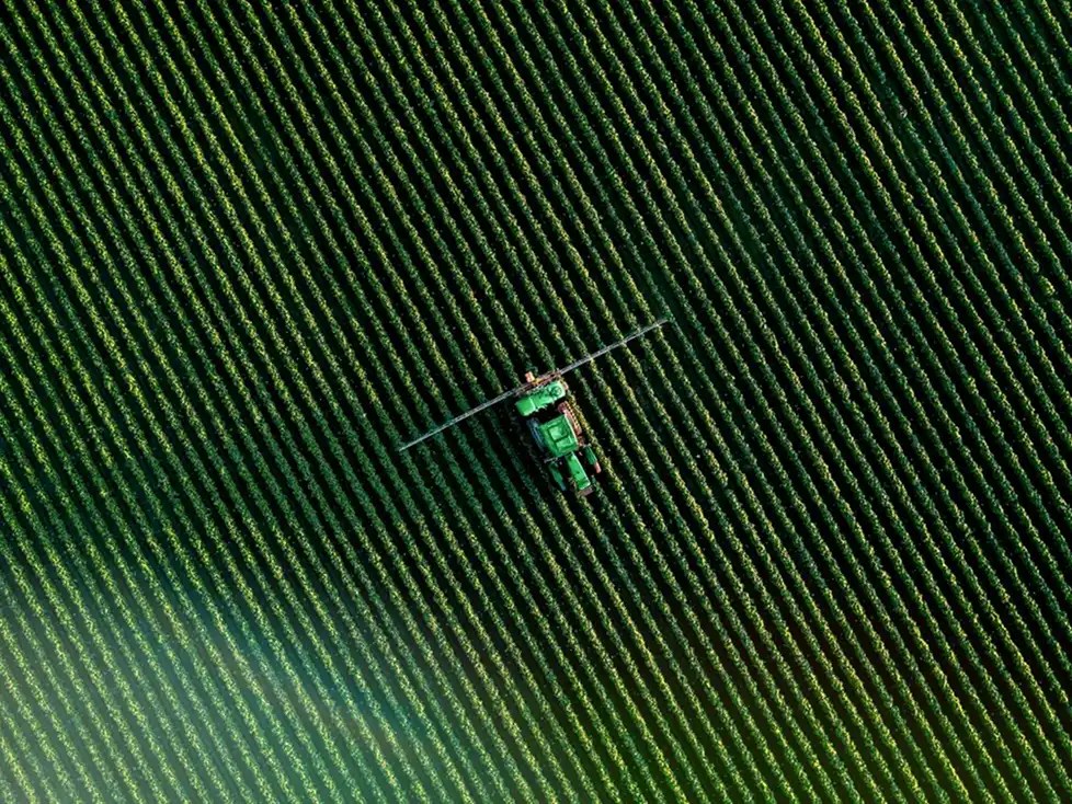 Aerial view of a green tractor spraying crops in a field.
