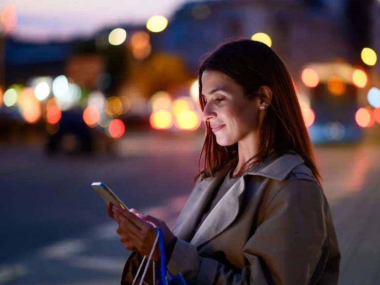 A woman standing near the street looking down at her phone