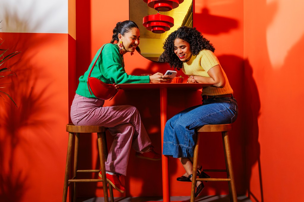 Two women sitting together and both looking at a mobile device