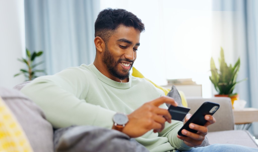 Male looking at phone while holding a credit card in hand