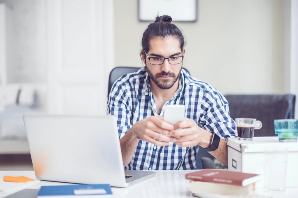 Man working at desk with his phone and laptop